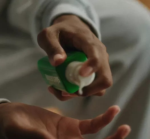 A close-up of a person's hands dispensing white lotion or soap from a green bottle into another hand.